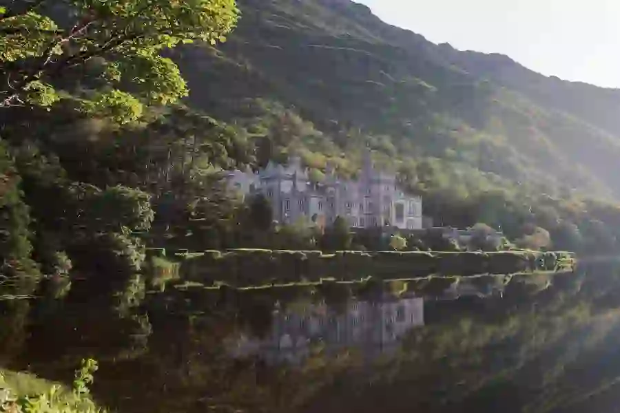 Kylemore Abbey in County Galway reflected in still water, surrounded by trees and green hillside.