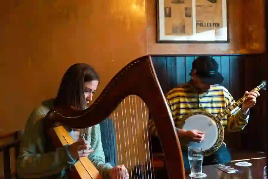 Musicians playing harp and banjo in a cosy Irish pub setting with wooden panelling.
