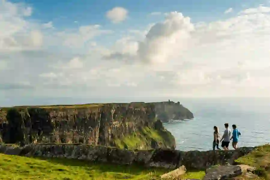 Group of people walking along the edge of the Cliffs of Moher in County Clare on a clear day.