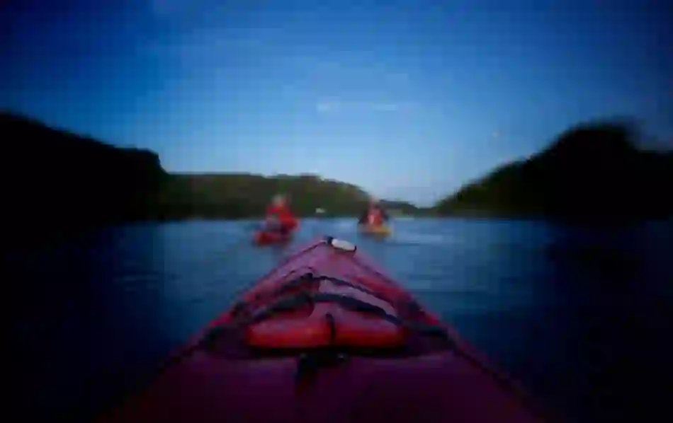 View from a red kayak at twilight on Lough Hyne in County Cork, with other kayakers paddling ahead between forested hills.