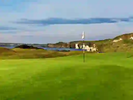Flag on the green at Royal Portrush Golf Club overlooking cliffs and the Atlantic Ocean.