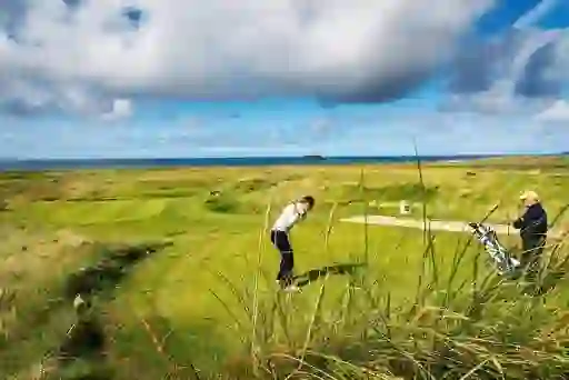 Golfer preparing to swing at Ballyliffin Golf Course with Atlantic Ocean views beyond the dunes.