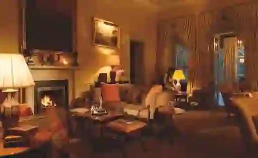 Luxurious lounge with a glowing fire, plush sofas and warm ambient lighting at Ballynahinch Castle Hotel, County Galway.