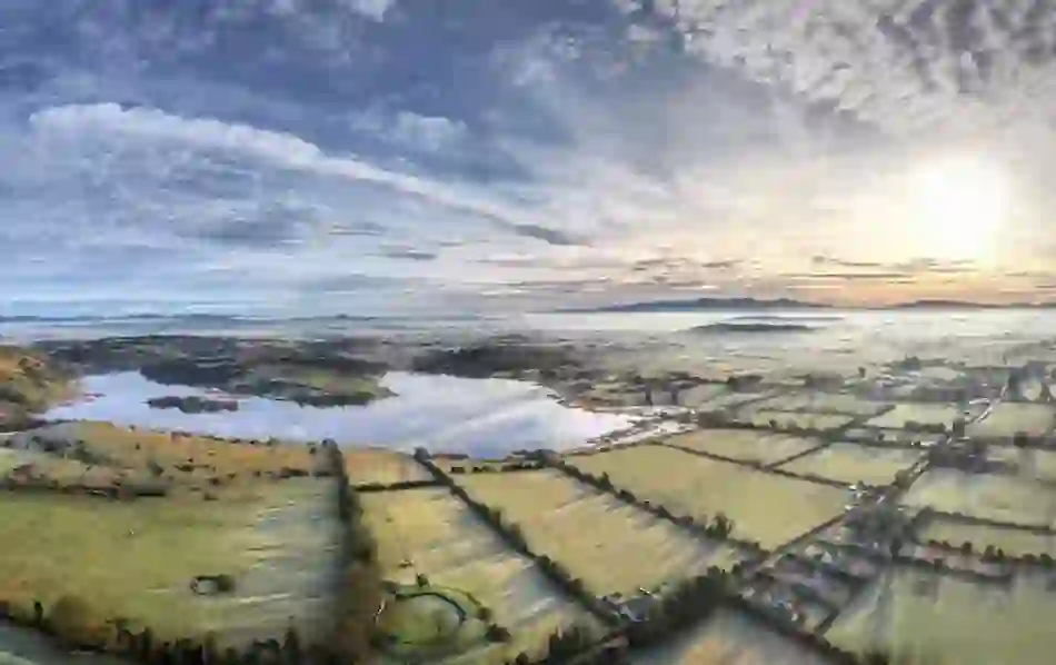 Lough Gur glistens in the soft light of winter with frosted fields and distant hills.