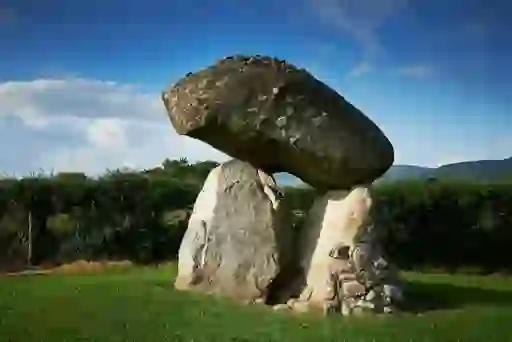 Megalithic portal tomb in County Louth with massive capstone balanced on upright stones against a clear blue sky.