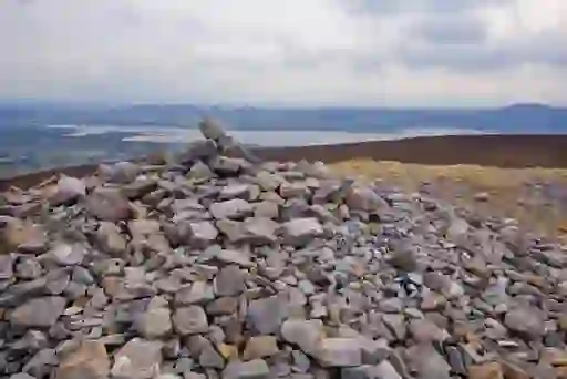 Stone cairn atop Knocknarea mountain overlooks coastal inlets and countryside in County Sligo under overcast skies.