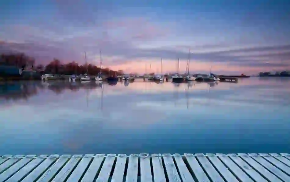 Yachts rest in Lough Neagh at Ballyholme Marina near Bangor at dusk, with pink-tinged skies reflected in the still harbour.