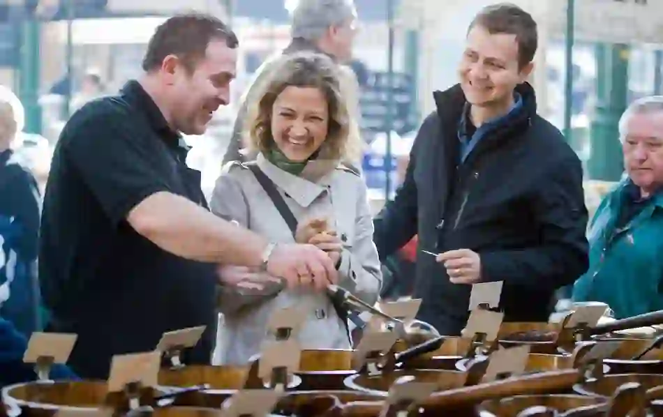 Smiling visitors chat with a vendor at St George’s Market in Belfast, browsing artisan goods in a lively indoor setting.
