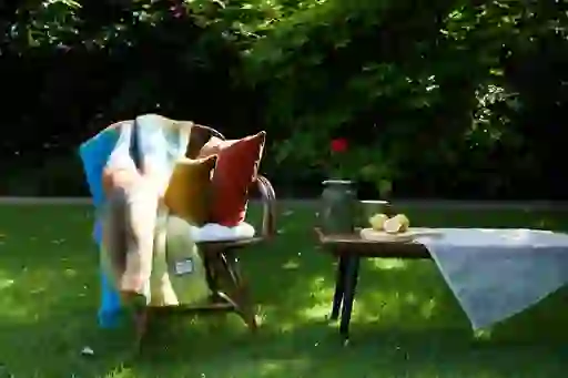 Colourful mohair throw draped over a wicker chair with cushions beside a garden table set with lemons and a vase.