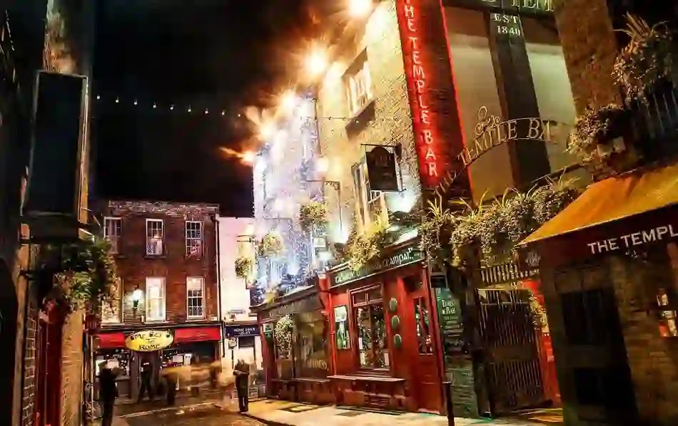 Temple Bar street at night with pubs lit by fairy lights and neon signs.