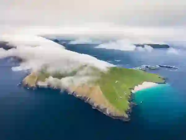 Low cloud sweeps over the Blasket Islands, County Kerry, revealing green fields, a sandy beach and turquoise Atlantic water.