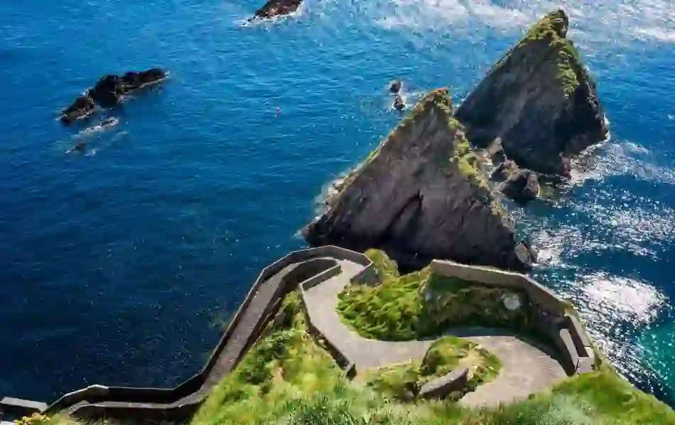Aerial view of the winding Dunquin Harbour path above deep blue Atlantic waters and jagged sea stacks in County Kerry.