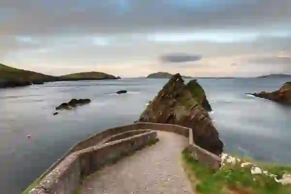 Curved stone pier at Dunquin Harbour leading to the sea, with sharp rocky outcrops and the Blasket Islands in the distance.