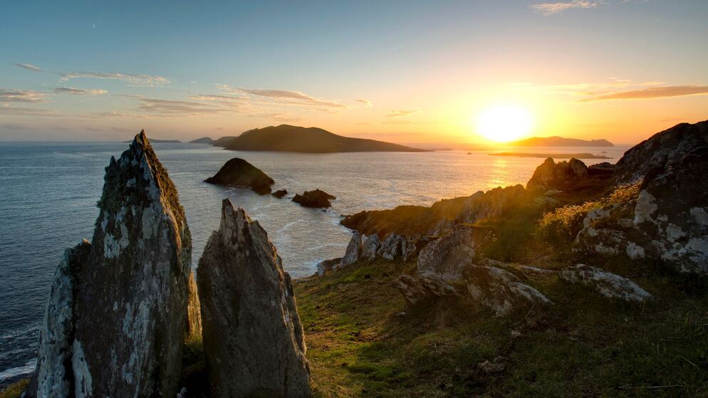 Sunset over the Blasket Islands, viewed from a rocky headland on the Dingle Peninsula, with jagged sea stacks in silhouette.