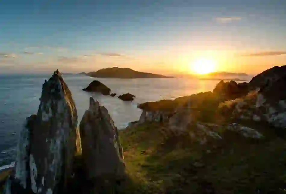 Sunset over the Blasket Islands, viewed from a rocky headland on the Dingle Peninsula, with jagged sea stacks in silhouette.