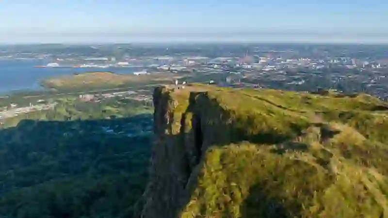 Clifftop viewpoint on Cave Hill, overlooking Belfast city and Belfast Lough, with walkers standing near the edge.