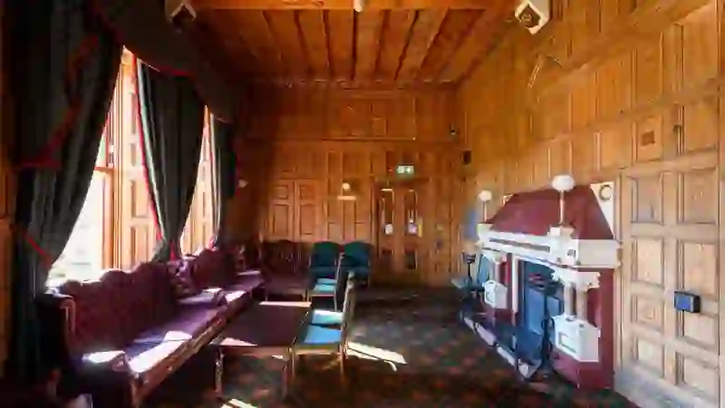 Wood-panelled drawing room at Belfast Castle with ornate fireplace, leather sofas and tall windows overlooking the grounds.