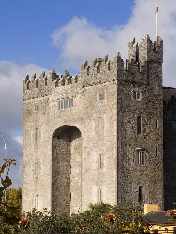 Bunratty Castle framed by autumn foliage, its stone towers rising above colourful leaves under a bright sky.