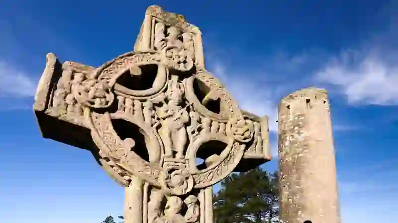 Close-up of a carved high cross at Clonmacnoise with a round tower in the background, County Offaly.