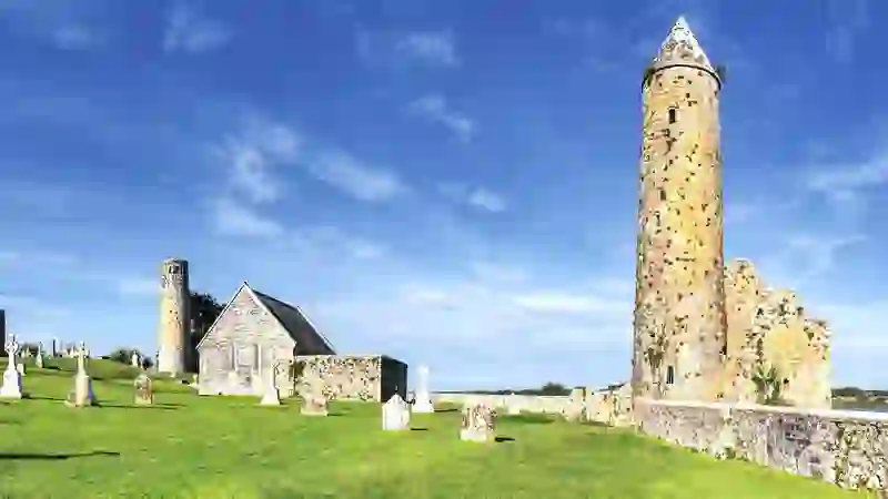 Clonmacnoise monastic site with round towers, church ruins and gravestones under a blue sky in County Offaly.