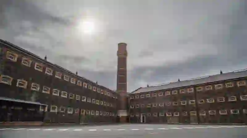 Exterior courtyard of Crumlin Road Gaol, Belfast, with stone walls, small windows and a tall brick chimney.