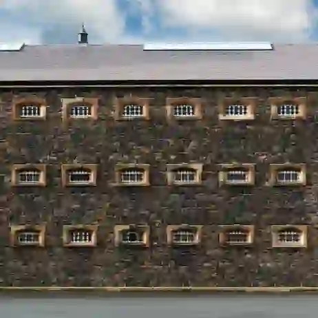 Stone exterior of Crumlin Road Gaol in Belfast, with rows of barred windows set into a dark stone façade.