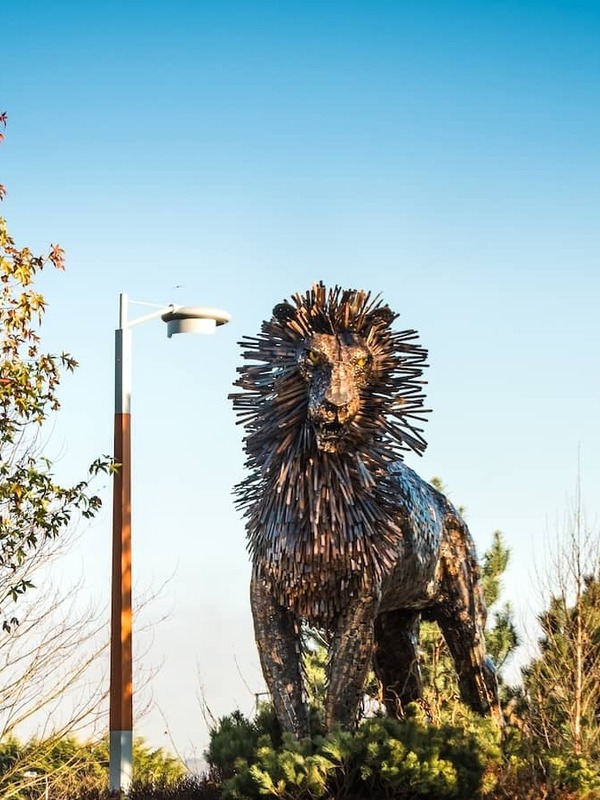 Large metal Aslan lion sculpture among trees at CS Lewis Square in Belfast.