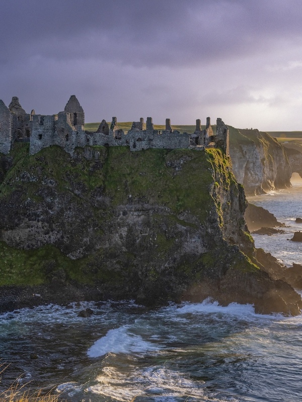 Dunluce Castle ruins perched on dramatic cliffs along the Causeway Coast at sunset.