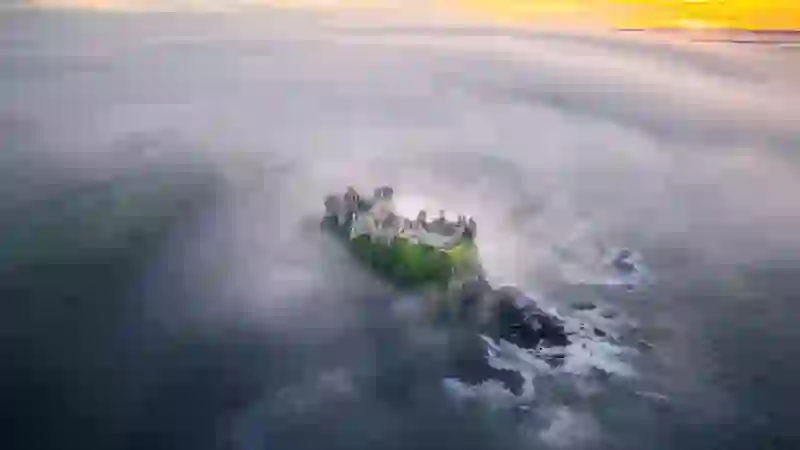 Aerial view of Dunluce Castle emerging through sea mist above the Atlantic Ocean.