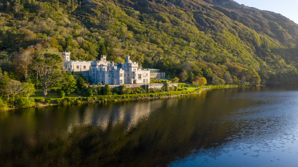 Kylemore Abbey reflected in Pollacappul Lake beneath wooded Connemara hills.