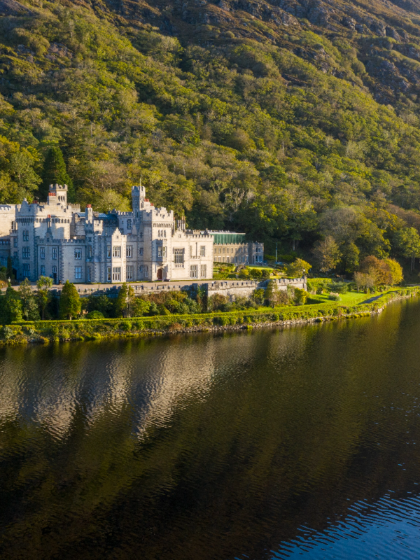 Kylemore Abbey reflected in Pollacappul Lake beneath wooded Connemara hills.