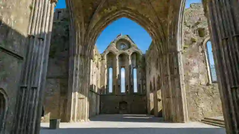 Inside the Rock of Cashel cathedral ruins, looking through a stone arch to tall Gothic windows.