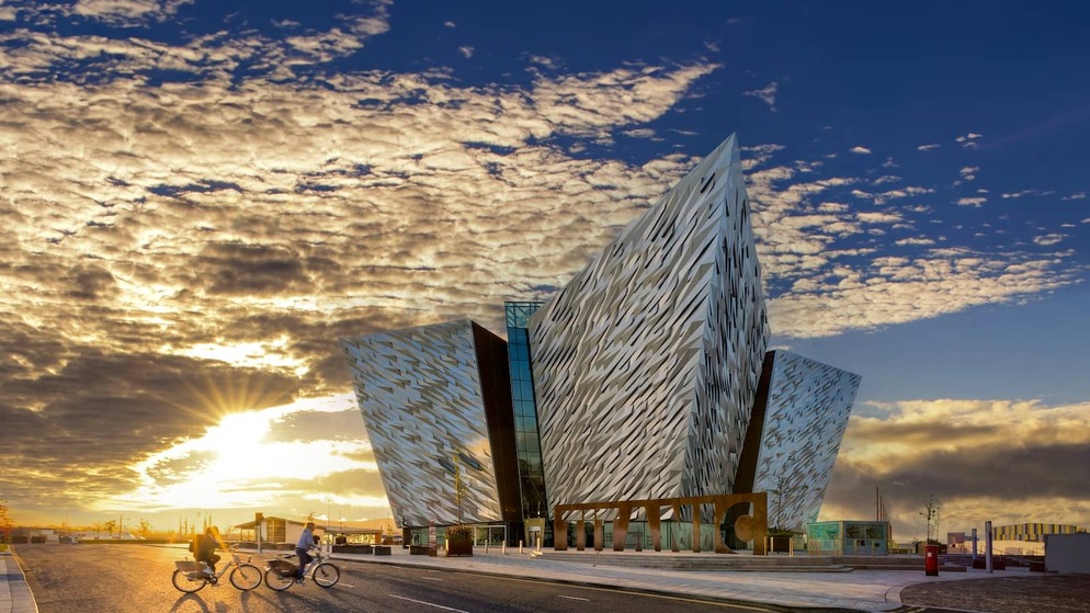 Cyclists passing Titanic Belfast at sunset, with golden light illuminating the building’s striking exterior.