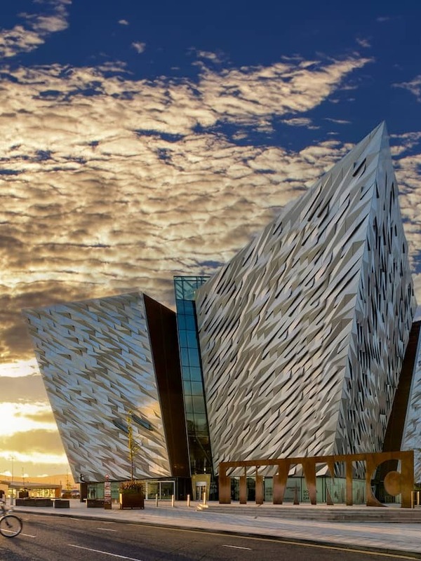 Cyclists passing Titanic Belfast at sunset, with golden light illuminating the building’s striking exterior.