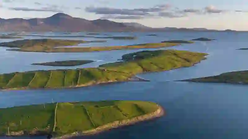 Aerial view of Clew Bay’s green islands with Croagh Patrick rising in the distance at sunset.