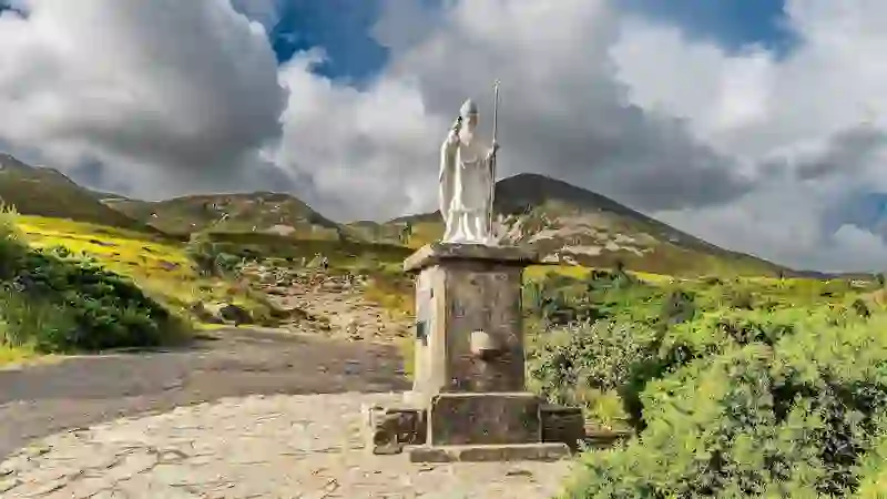 Statue of Saint Patrick at the base of Croagh Patrick with rugged mountains behind.
