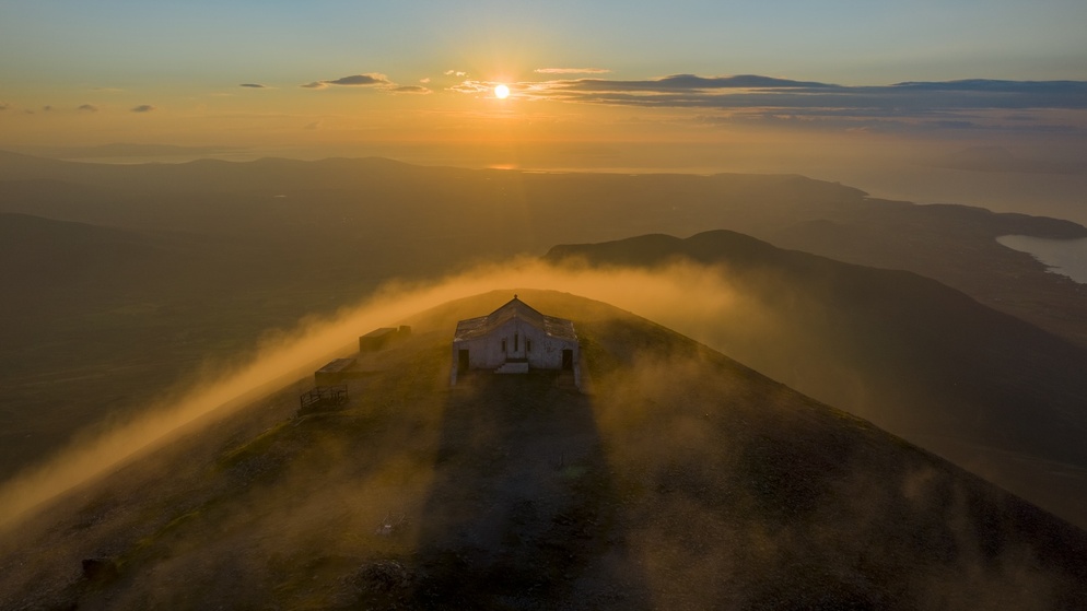 Sunset over Croagh Patrick summit, with the chapel surrounded by mist and golden light.