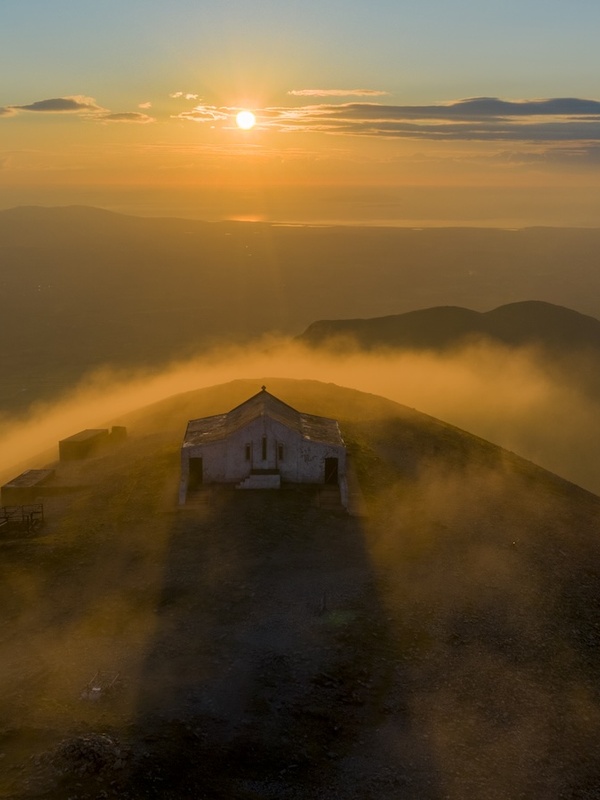 Sunset over Croagh Patrick summit, with the chapel surrounded by mist and golden light.