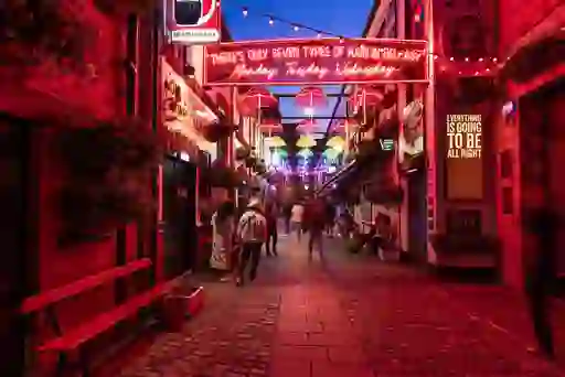 Commercial Court in Belfast lit with colourful umbrellas and neon signs as people stroll along the cobbled street at night.