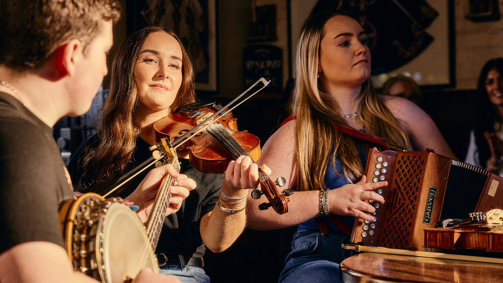 Traditional Irish music session with fiddle, banjo and accordion players performing in a cosy Belfast pub.