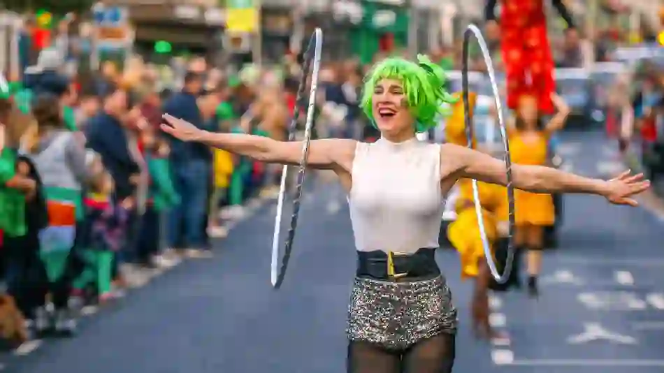 Three performers in colourful wigs and painted faces smile during a St Patrick’s Day parade in Ireland.