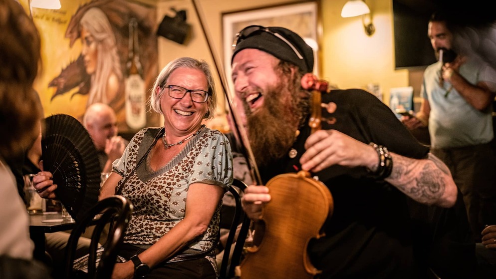 Musician laughing with a woman during a lively traditional music session in McHugh's pub in Belfast.
