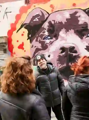 Guide chatting with visitors beside a vibrant dog mural in a Belfast alleyway during a street art tour.