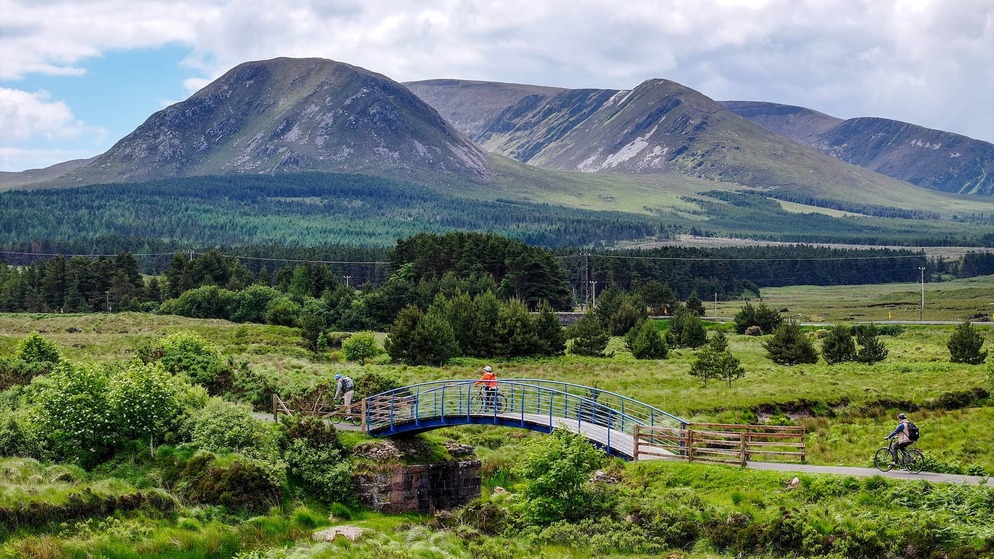 Cyclists cross a bridge on the Great Western Greenway with Croagh Patrick in County Mayo beyond.