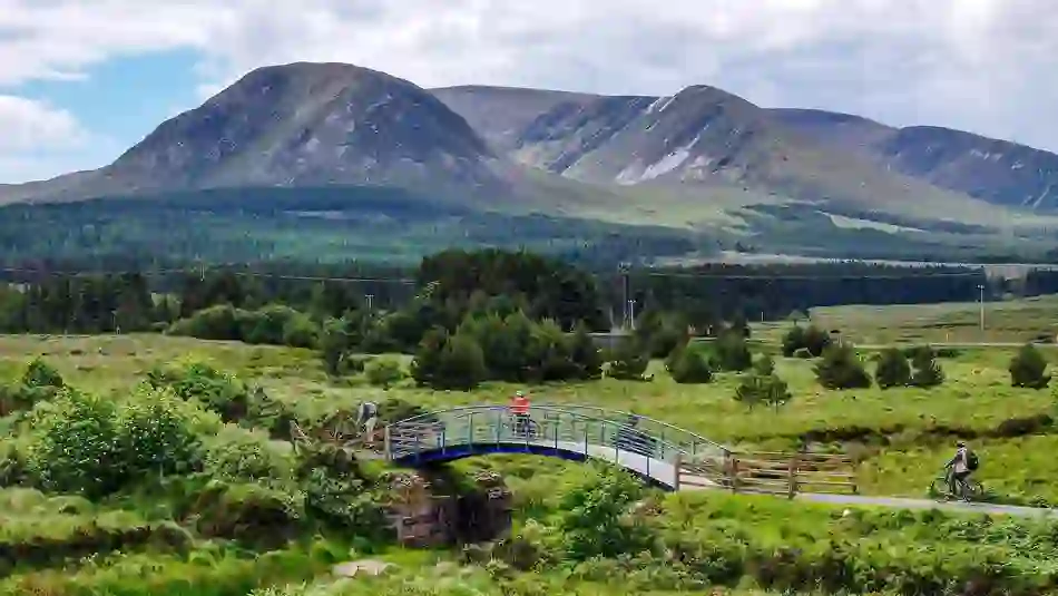 Cyclists cross a bridge on the Great Western Greenway with Croagh Patrick in County Mayo beyond.