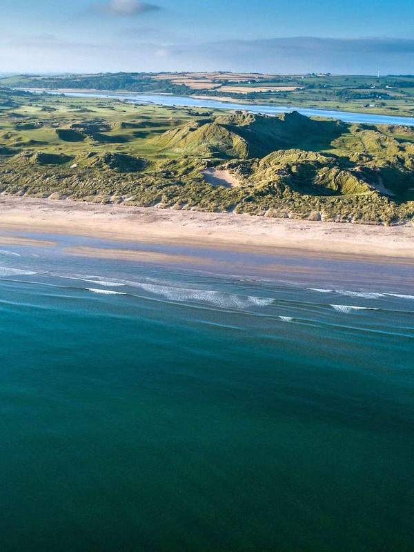 Aerial view of Portstewart Golf Club's links course beside a long sandy beach in County Londonderry.