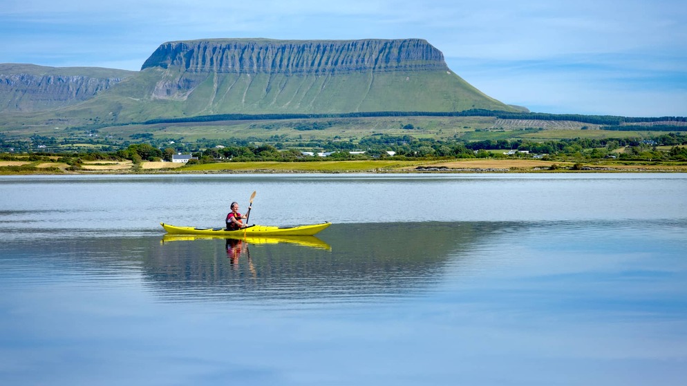Person kayaking on calm water with Benbulben mountain in the background, County Sligo.