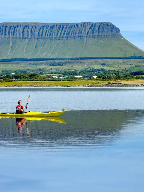 Person kayaking on calm water with Benbulben mountain in the background, County Sligo.
