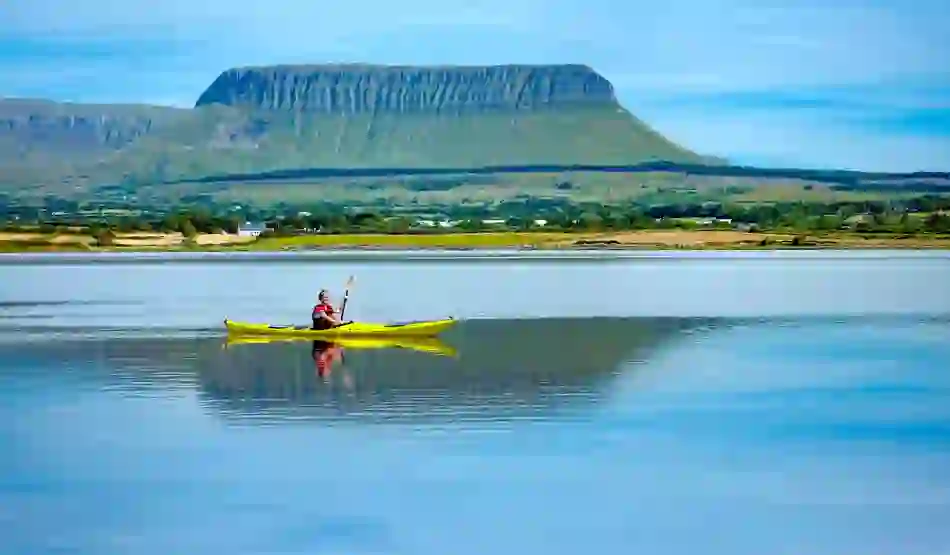 Person kayaking on calm water with Benbulben mountain in the background, County Sligo.
