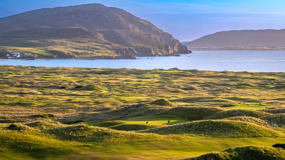 Golfers playing on the links at Ballyliffin Golf Club with rugged coastline in County Donegal.